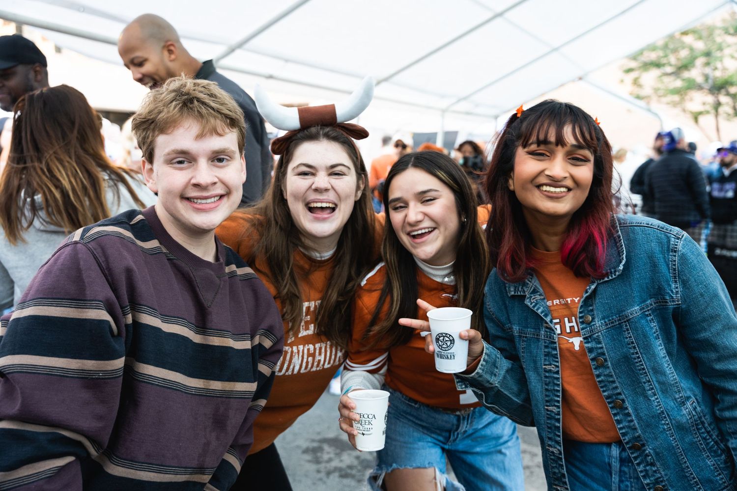 Students smiling for a group photo during a university event under a tent.