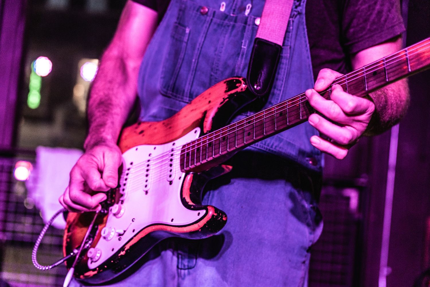 Close-up shot of electric guitar being played under purple stage lighting.