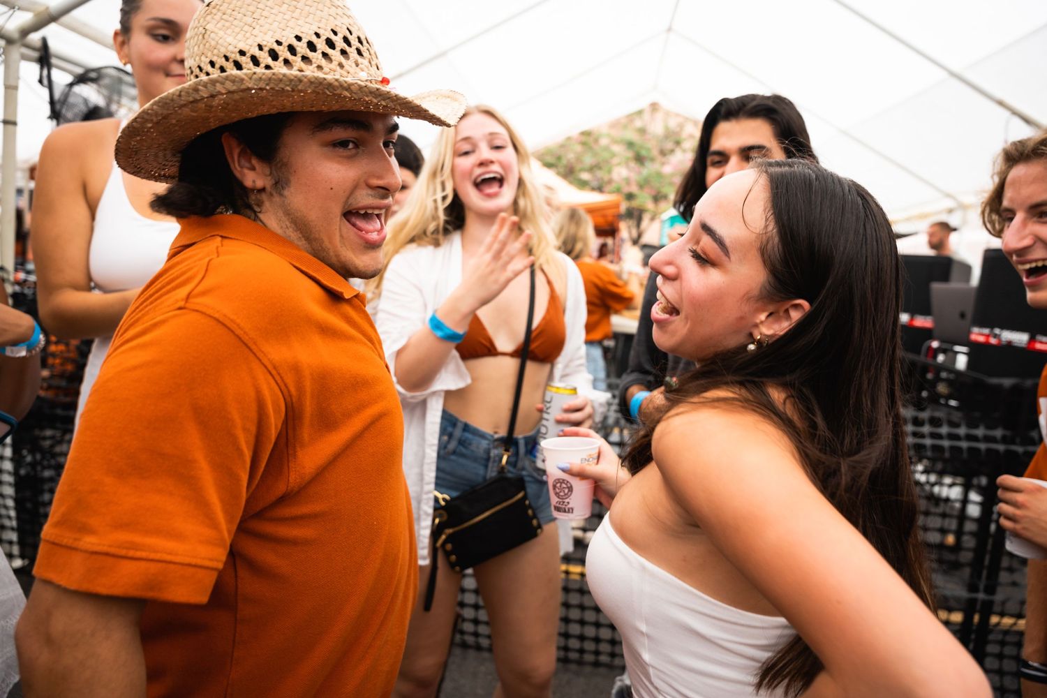 Group laughing and socializing at outdoor party under white tent.
