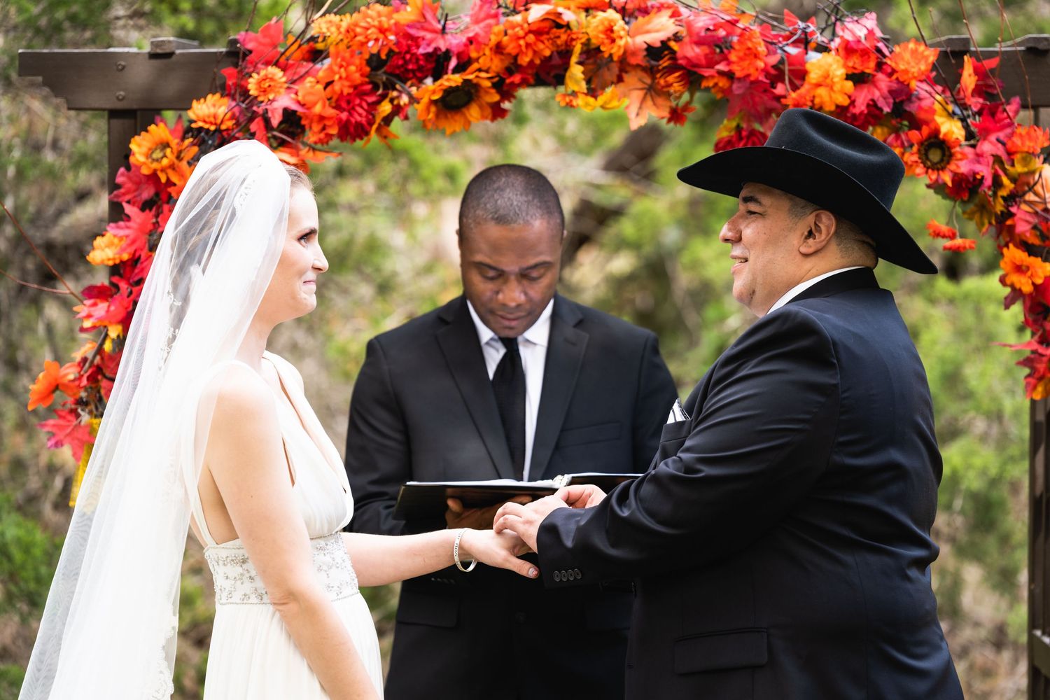 An exchange of rings during a wedding ceremony beneath a colorful floral archway.
