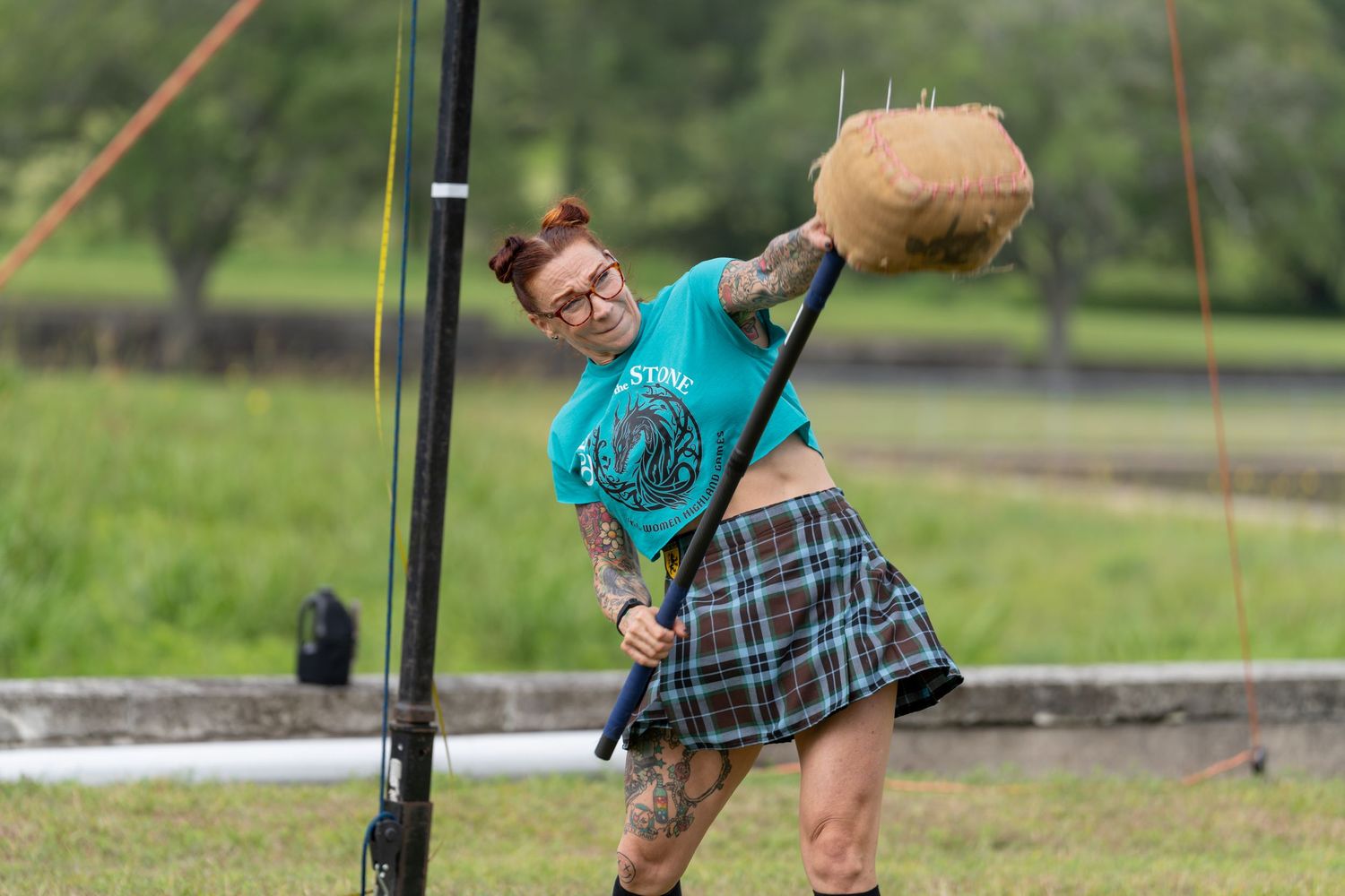 Woman in tartan kilt competes in Highland Games hammer throw event outdoors.