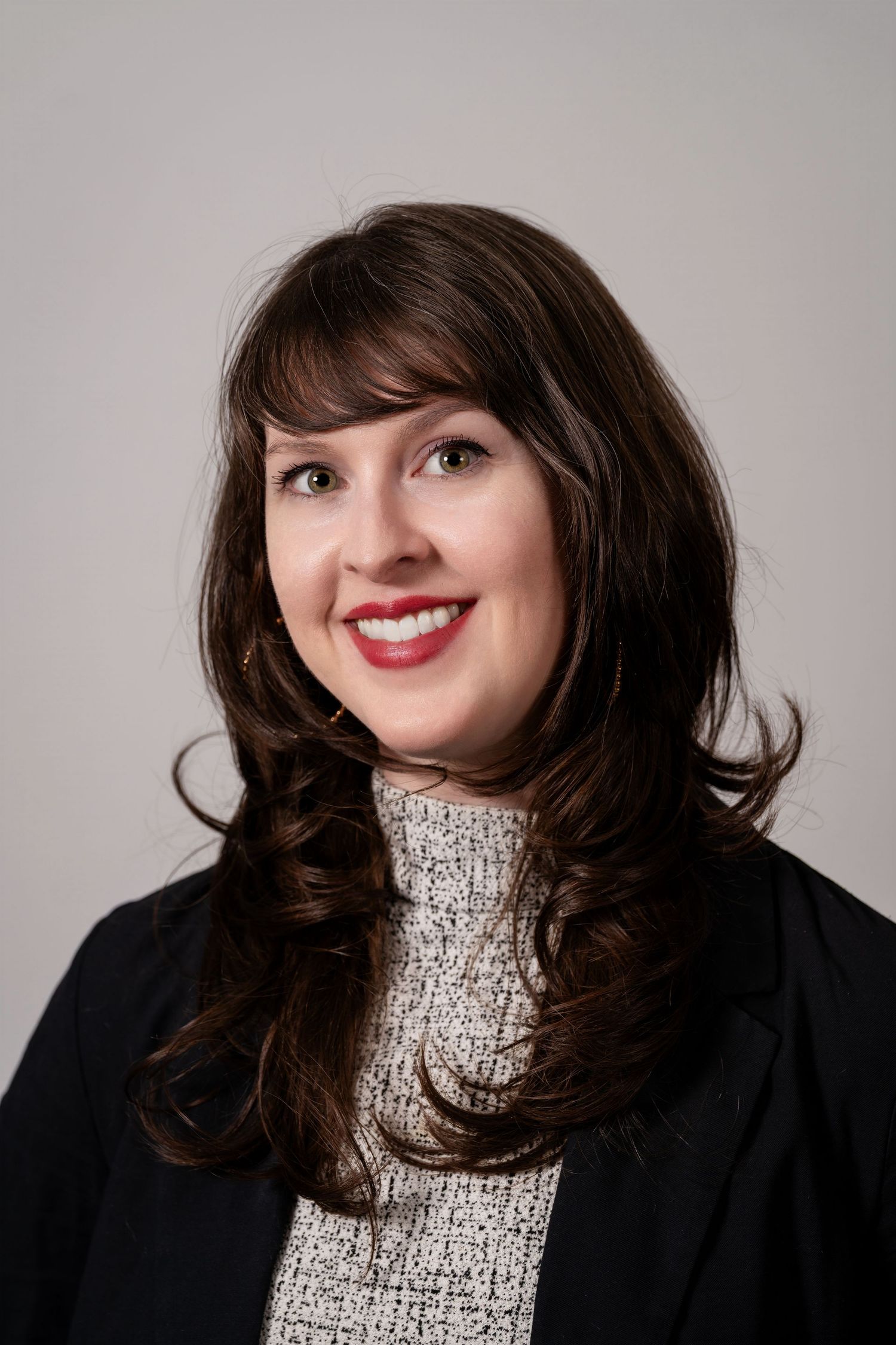 Professional headshot of a smiling woman with dark hair, wearing a black blazer and patterned top.