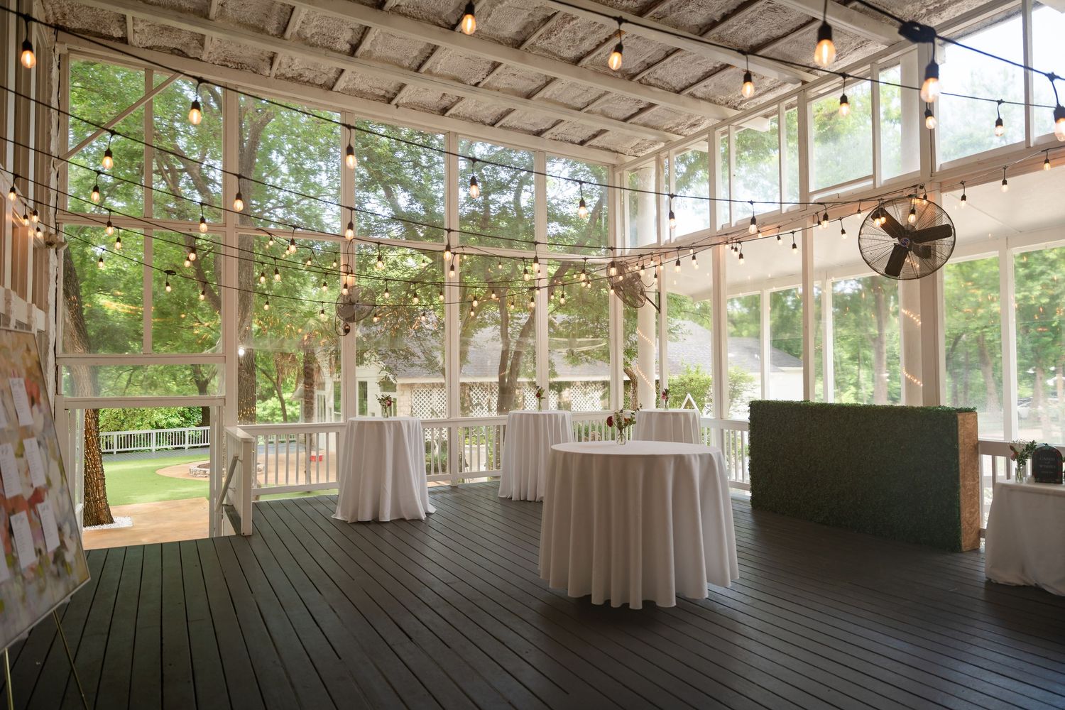 Elegant covered patio venue with string lights, white draped cocktail tables, and lush garden views for weddings.