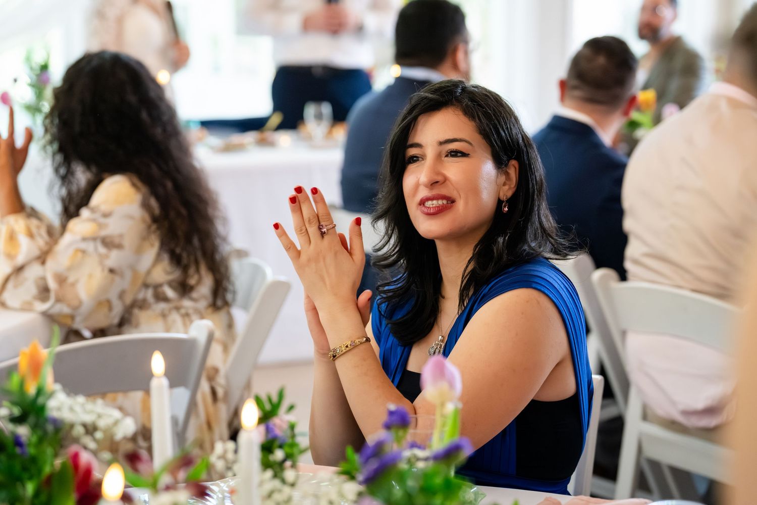 Woman in blue dress clapping at elegant wedding reception table with floral centerpieces.