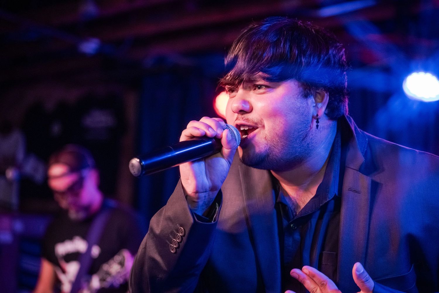 A performer sings into a microphone on stage with blue lighting in the background during a live music show.