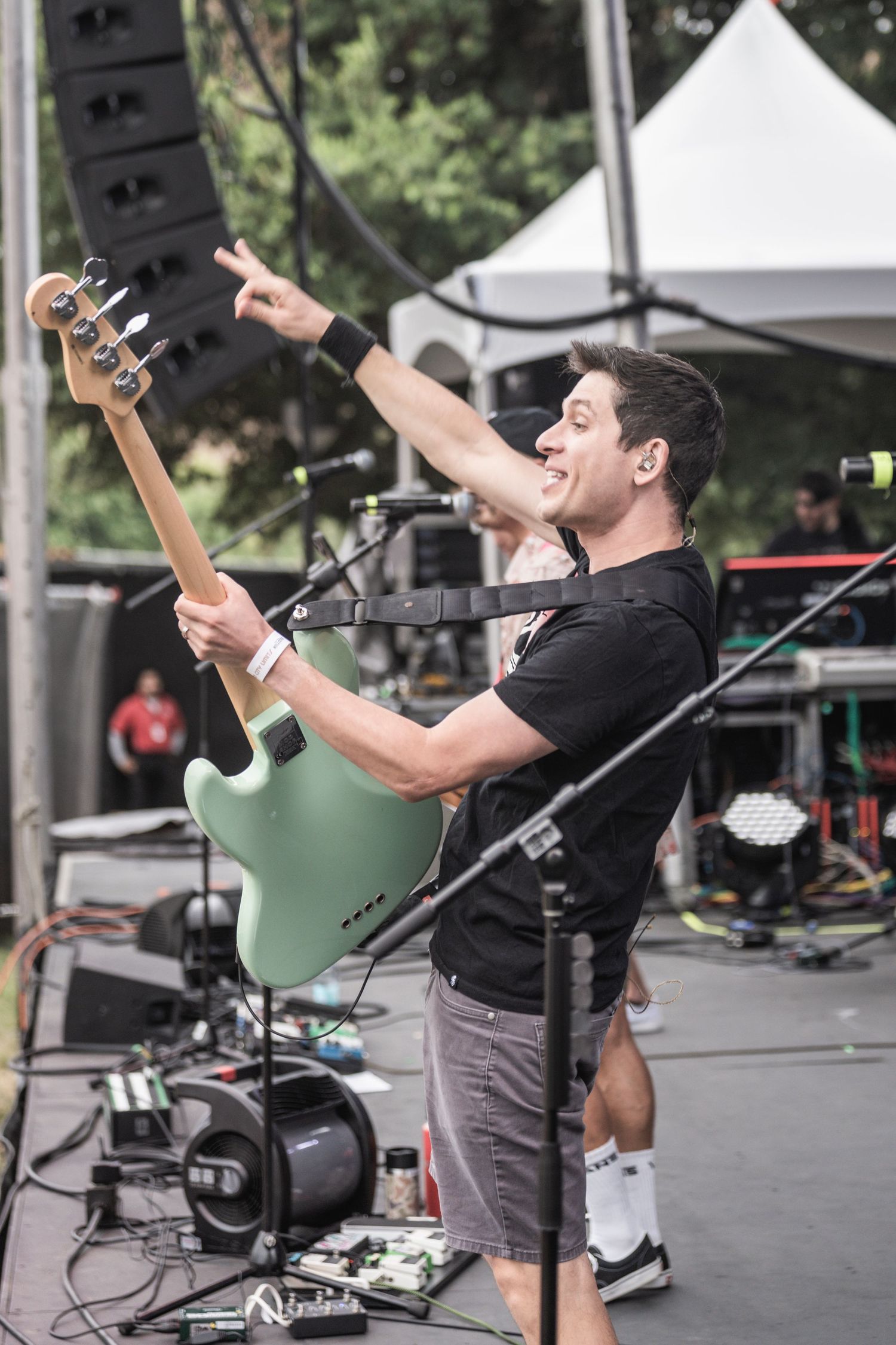 Energetic musician performs on stage at outdoor concert venue with guitar and microphone setup.