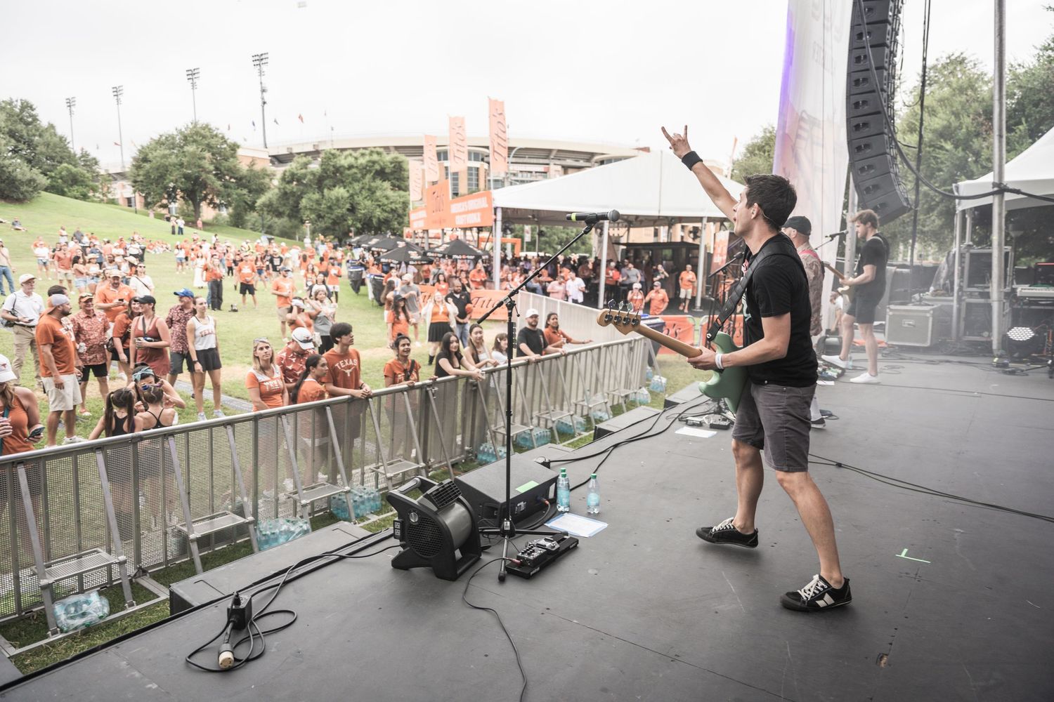 A performer on stage points to a large crowd of festival attendees behind metal barriers during an outdoor concert.