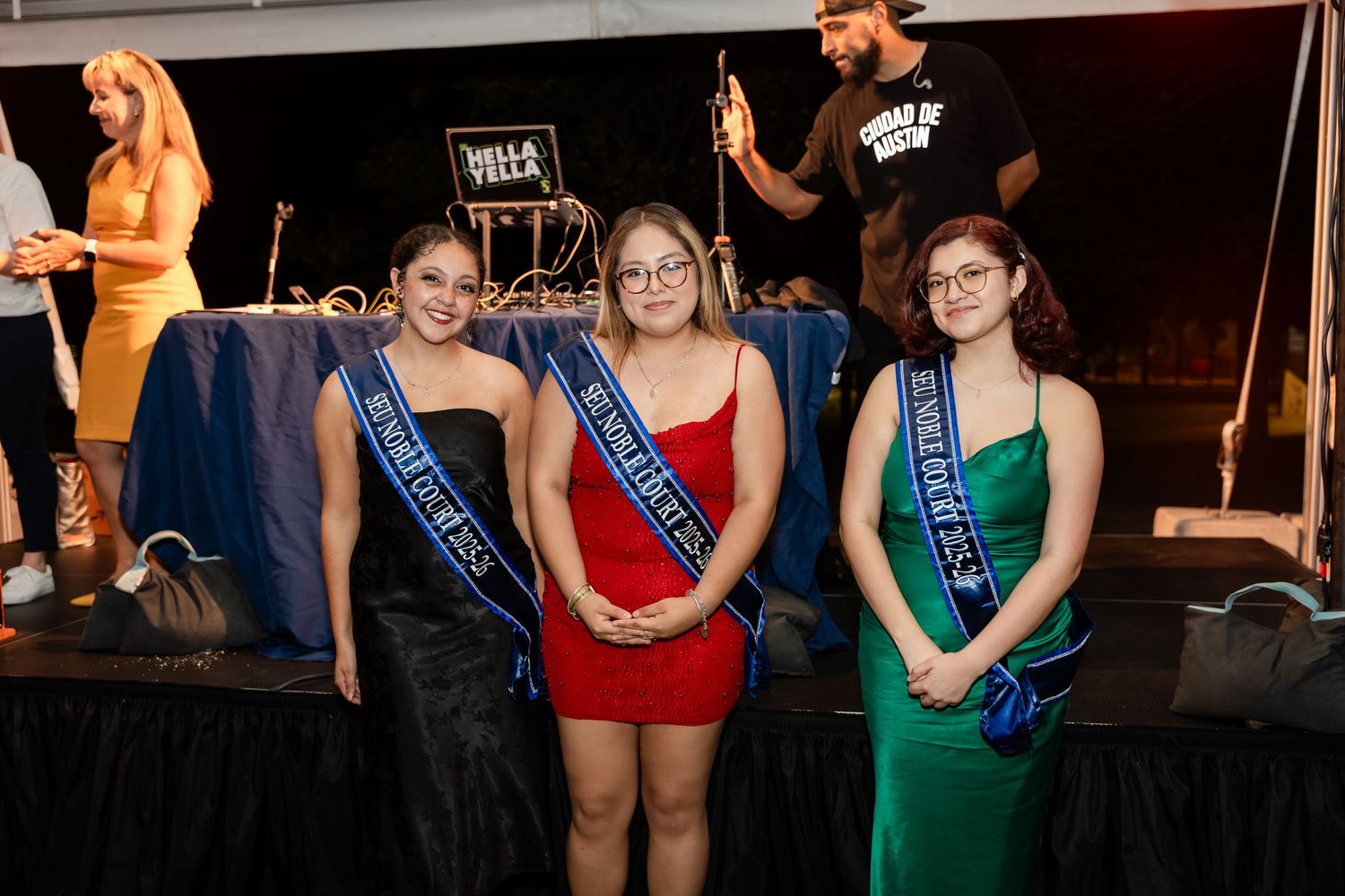 Beauty pageant contestants in colorful evening gowns stand together on stage during competition.