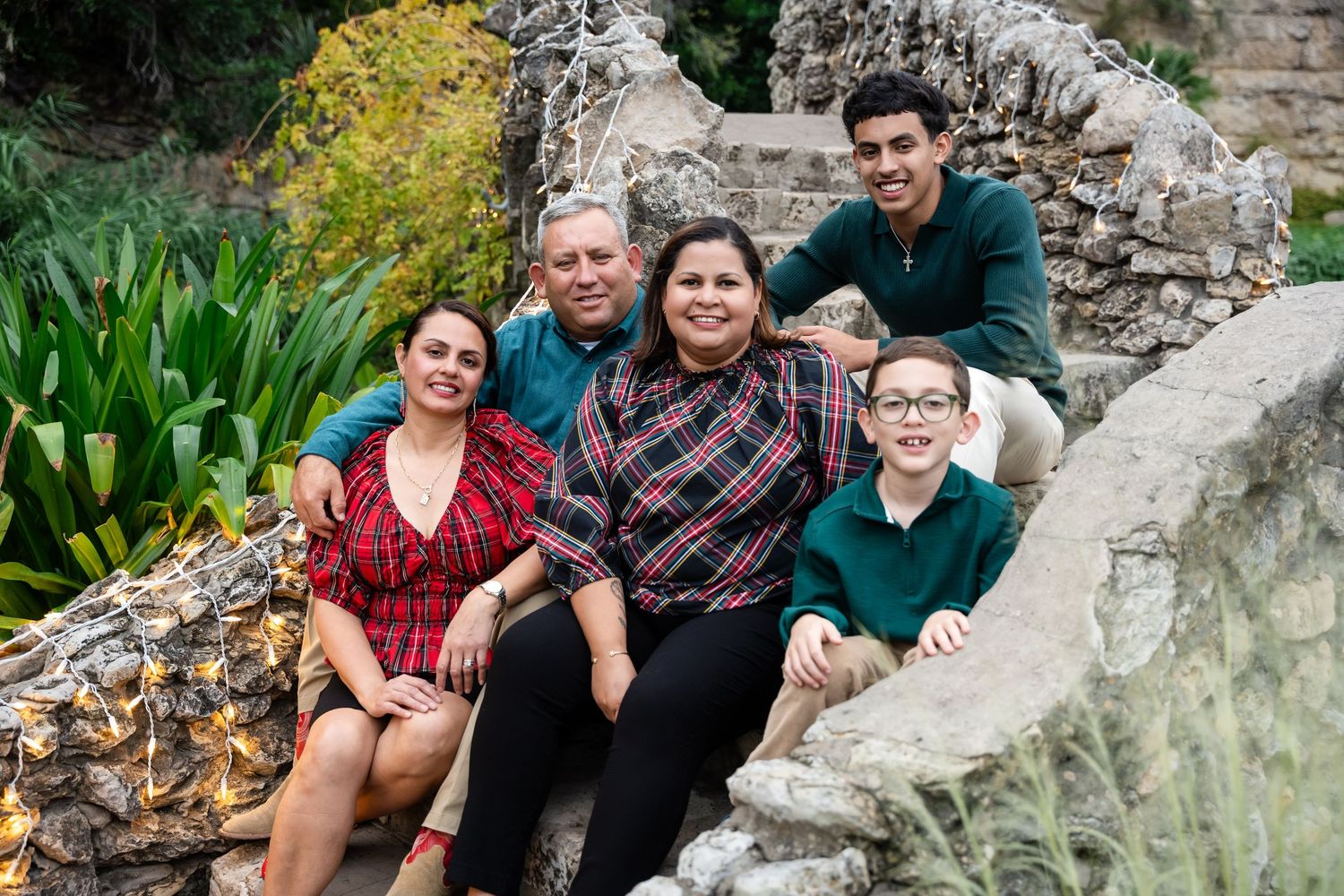 A group sits together on stone steps surrounded by greenery and garden landscaping at an outdoor location.