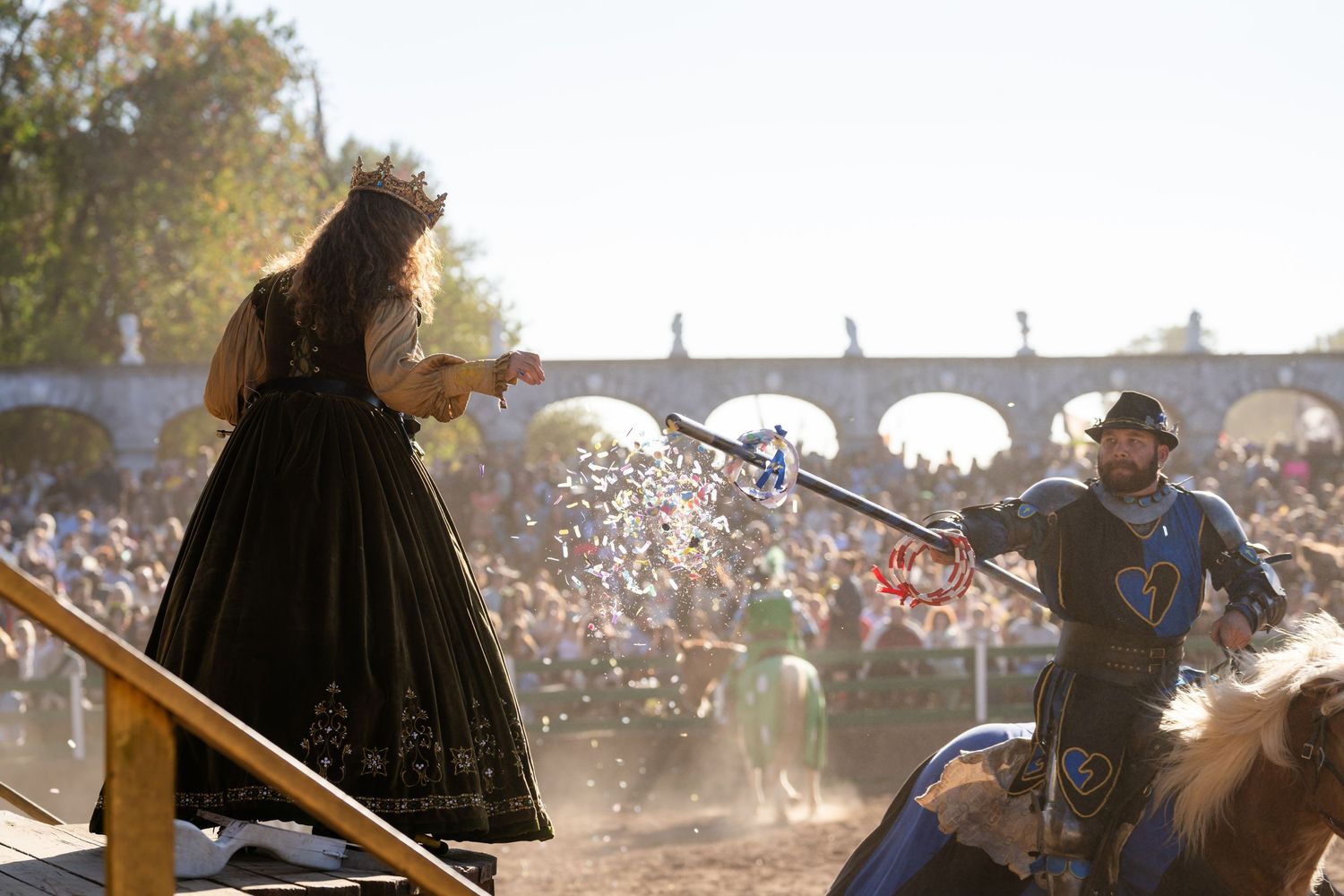 A panoramic view of a rodeo arena with riders and spectators gathered under a bright sunny sky.
