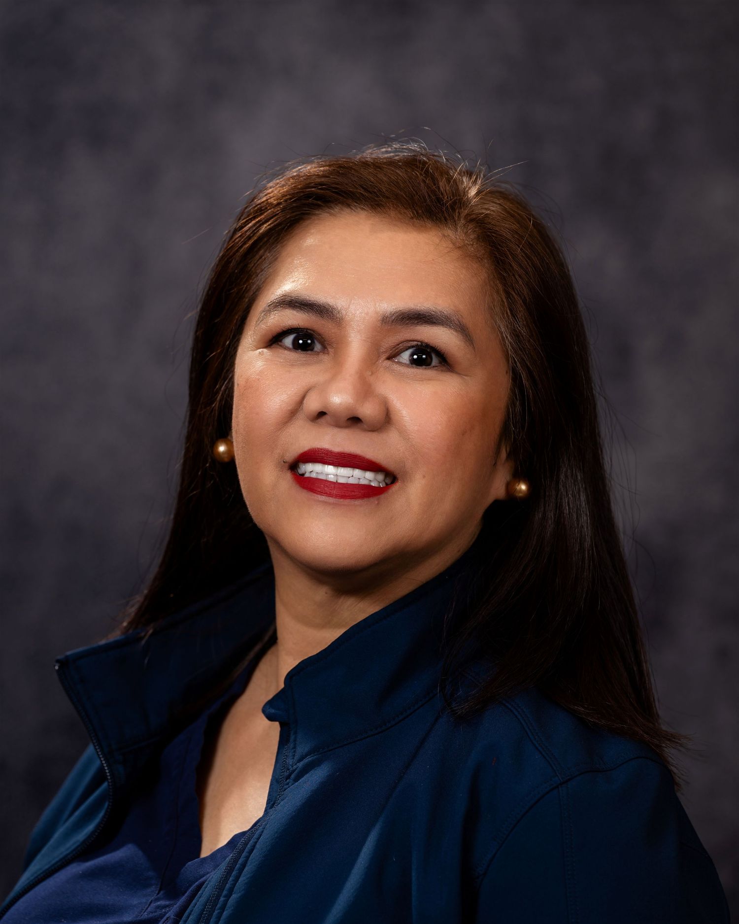 Professional headshot portrait in navy blazer against dark background with warm smile and polished appearance.