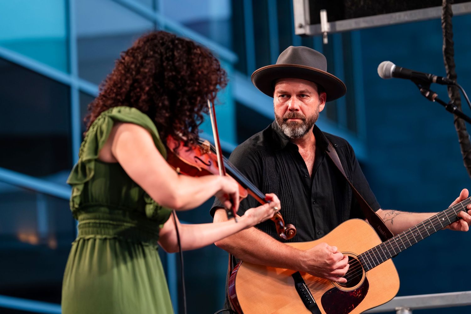 Musicians perform on stage with acoustic guitars at a concert with blue lighting and professional sound equipment.