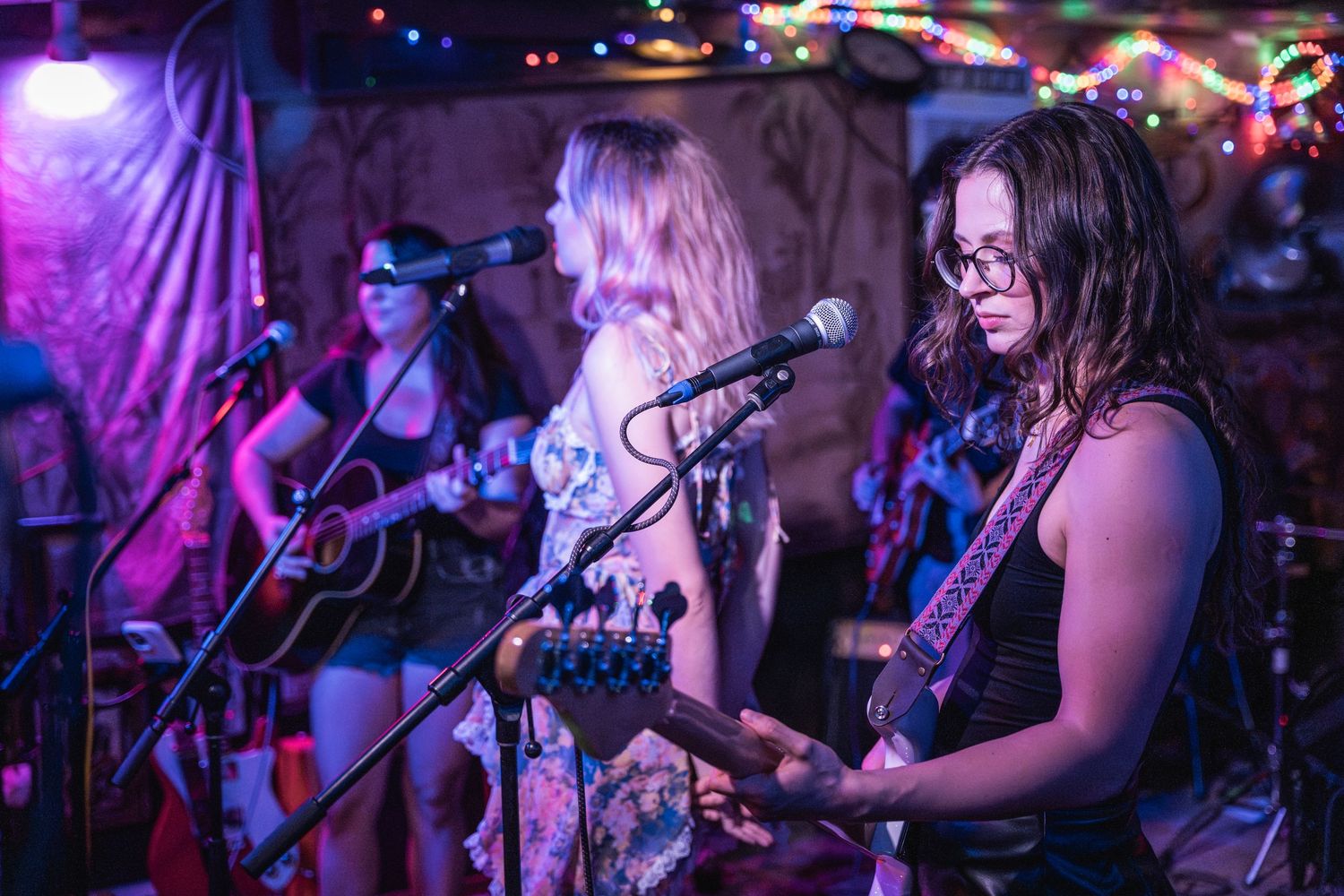 Musicians perform on stage with guitars under purple lighting at a live music venue.