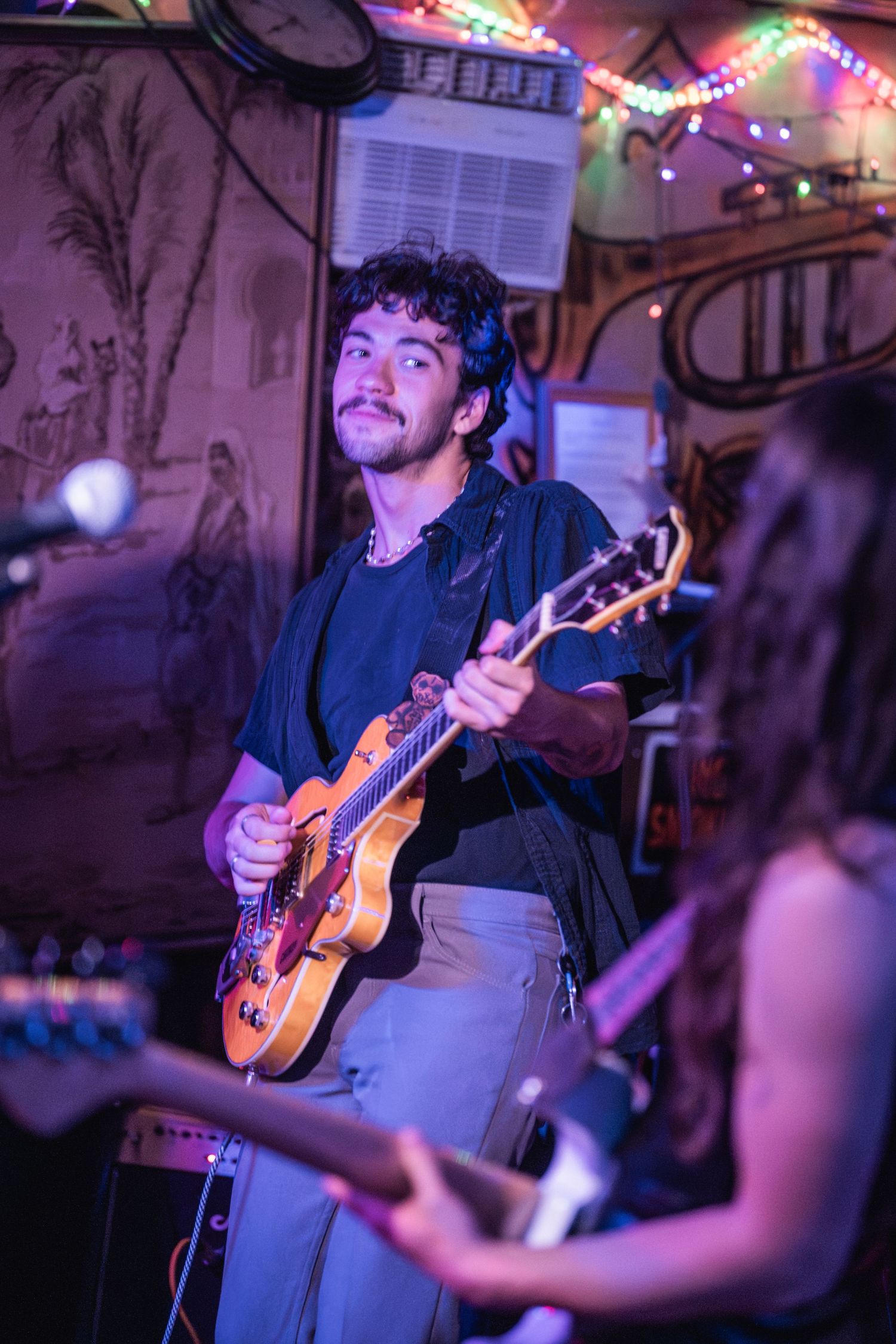 Musician performs on acoustic guitar under purple stage lighting at intimate venue setting.