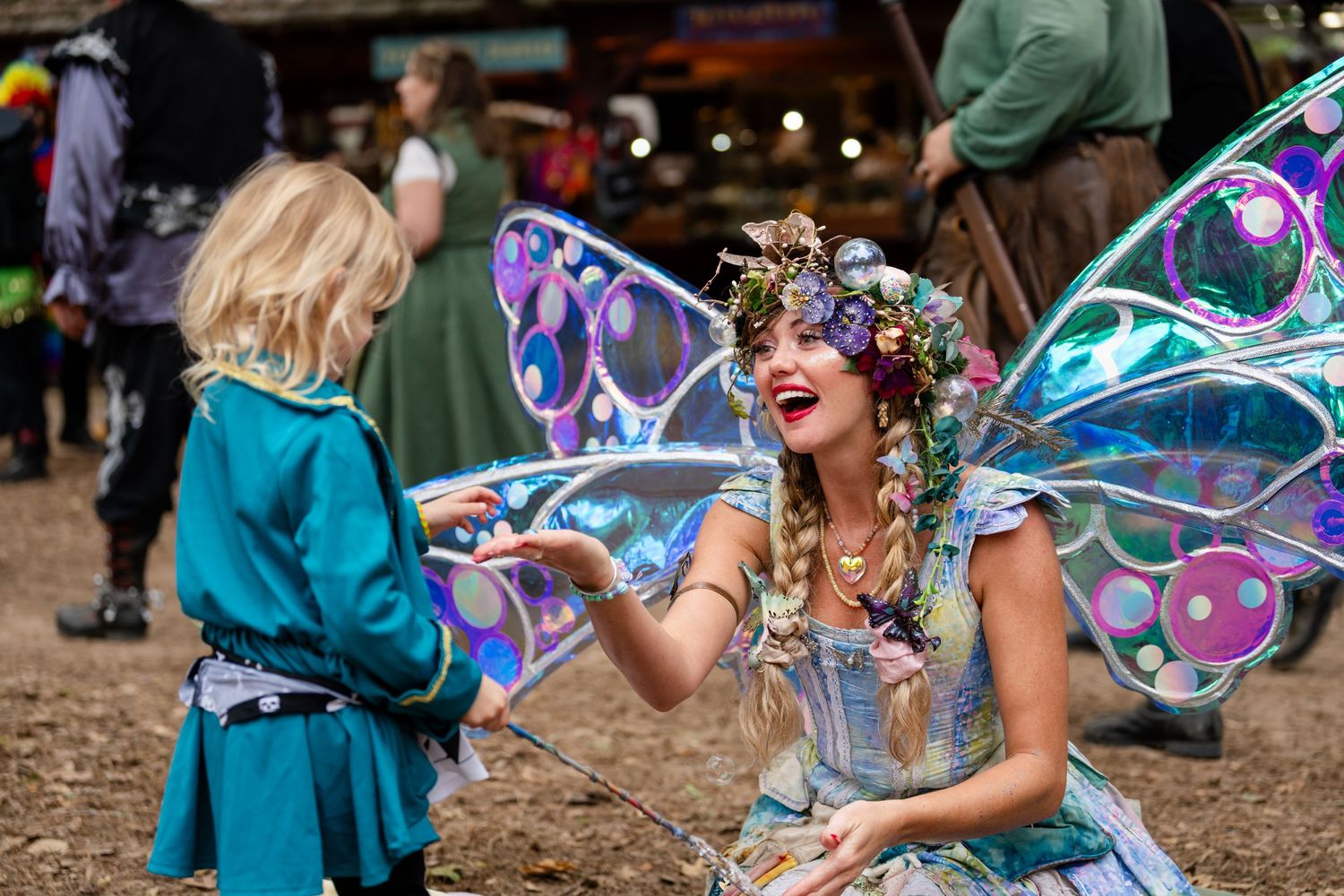 Giant iridescent bubbles float through the air at an outdoor festival as people play and interact with them.