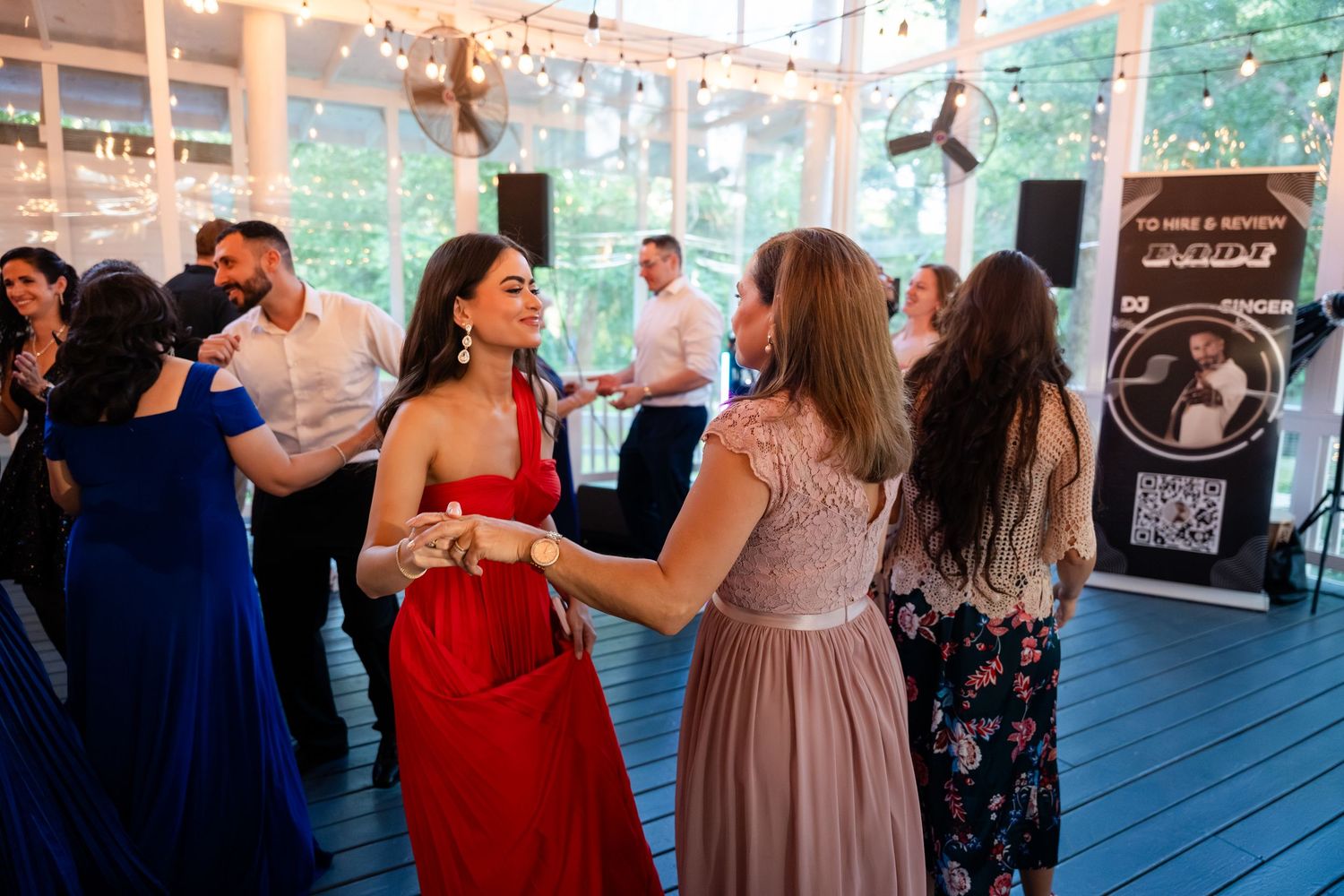 Guests dancing in formal attire at an elegant indoor wedding reception with string lights and wooden floors.
