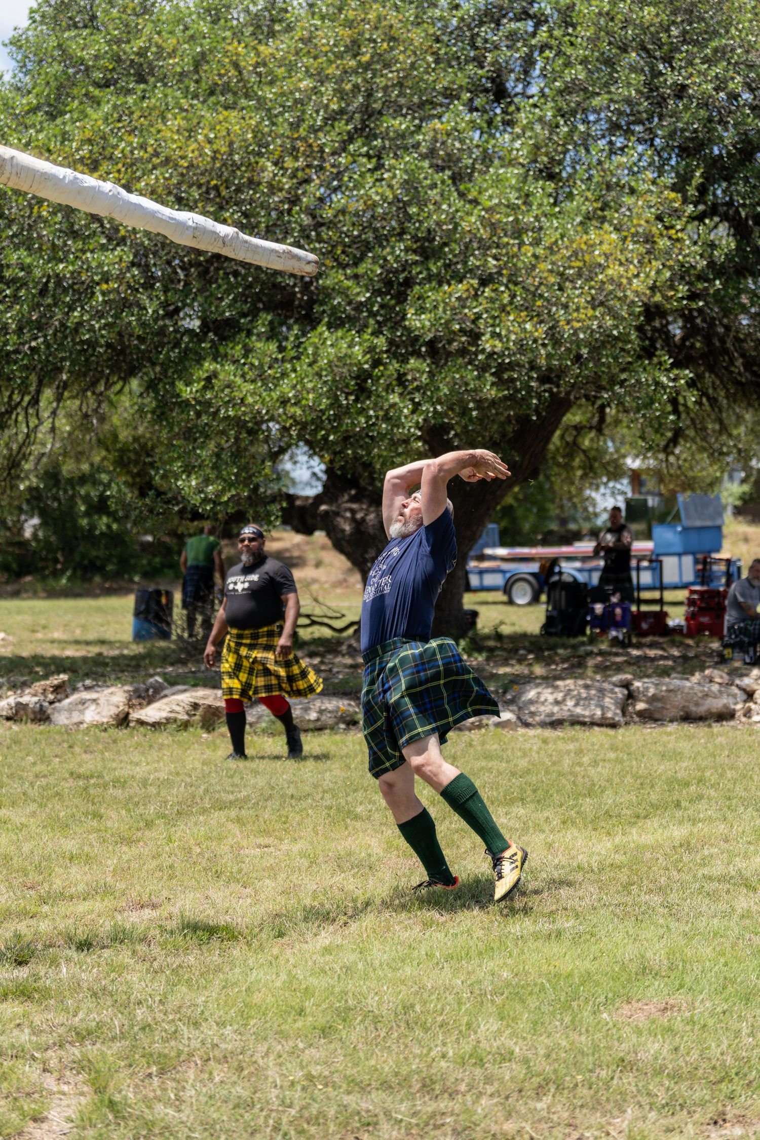 Man in tartan kilt tosses caber at Scottish Highland Games outdoors.