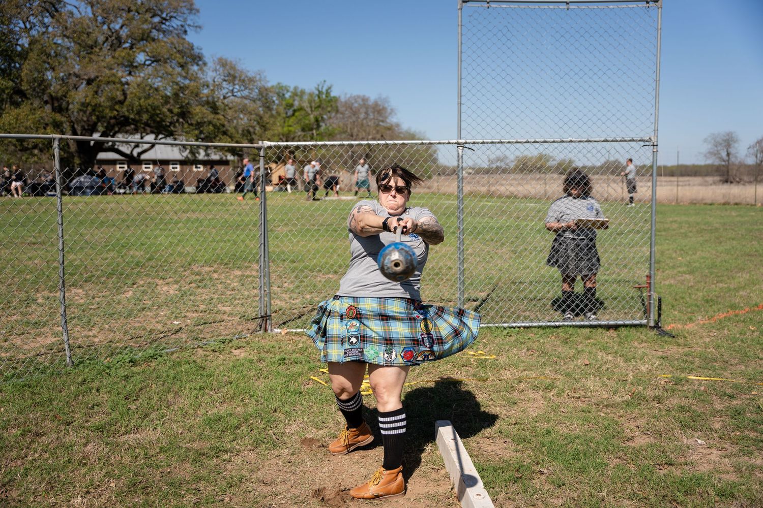 Man in tartan kilt performs hammer throw at Highland Games competition outdoors.