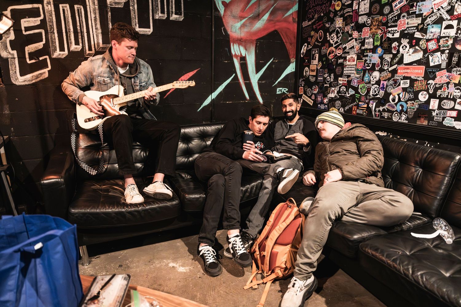 Band members relaxing on leather couches in a music venue green room.