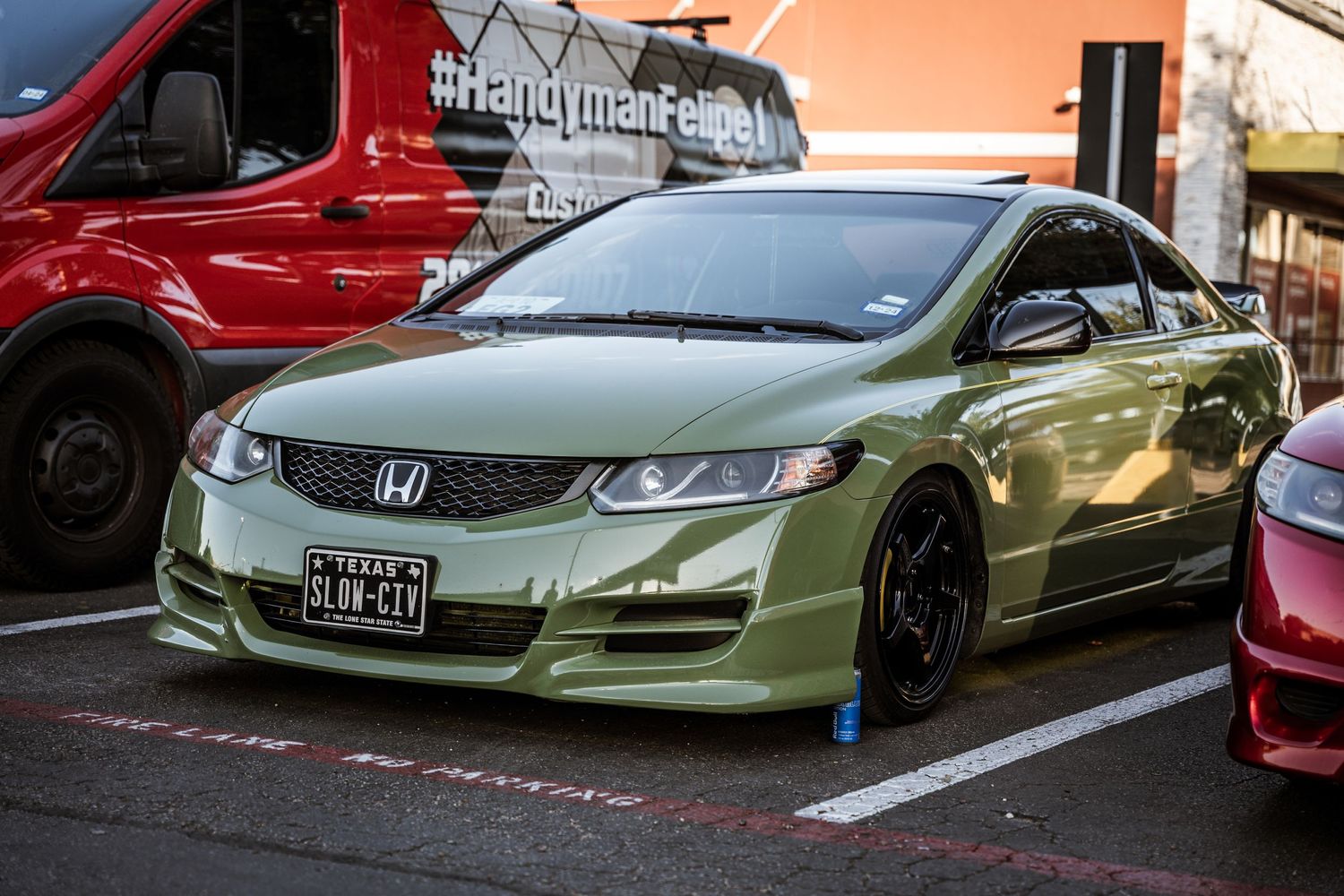 A modified green Honda Civic with custom wheels parked in a shopping center lot.