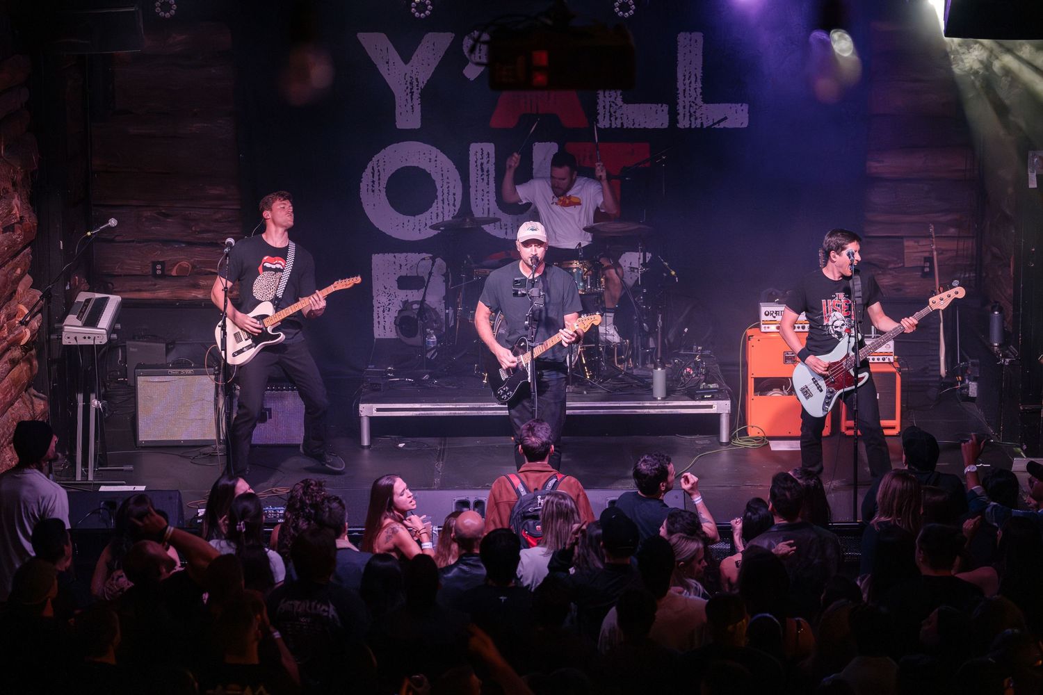 Musicians perform on stage with 'YOF' lettering visible in the background under blue lights.