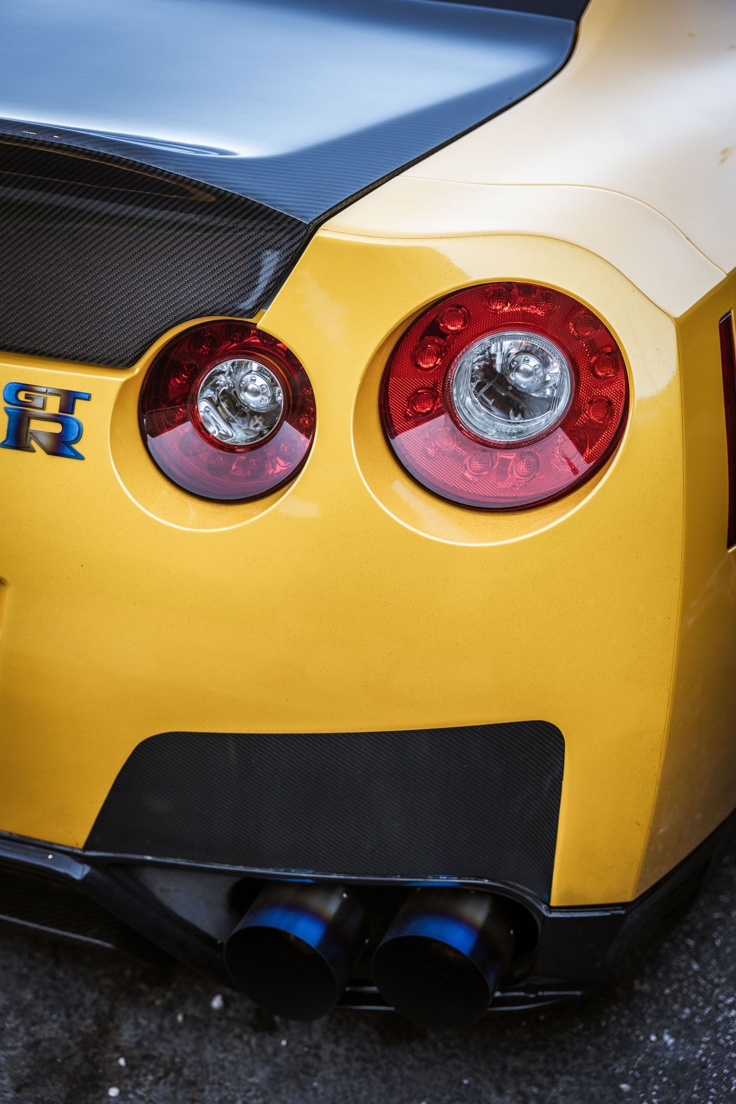 Close-up of yellow Nissan GTR rear taillights and carbon fiber details with blue exhaust tips.