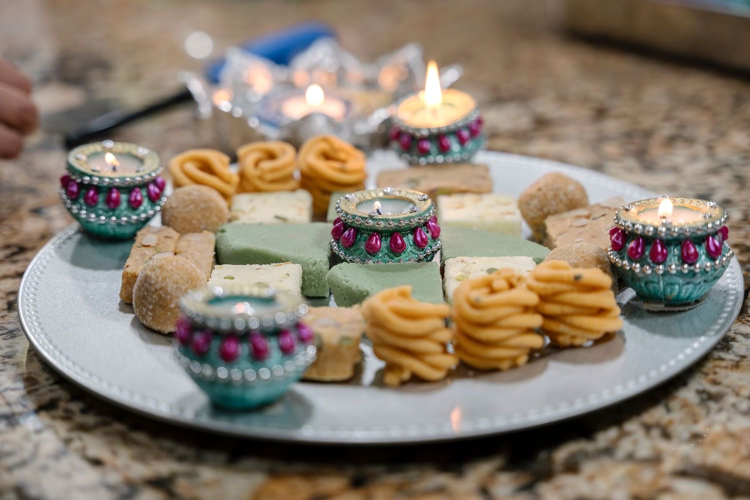 Traditional Indian sweets and decorative candles arranged on a silver platter for Diwali celebration.