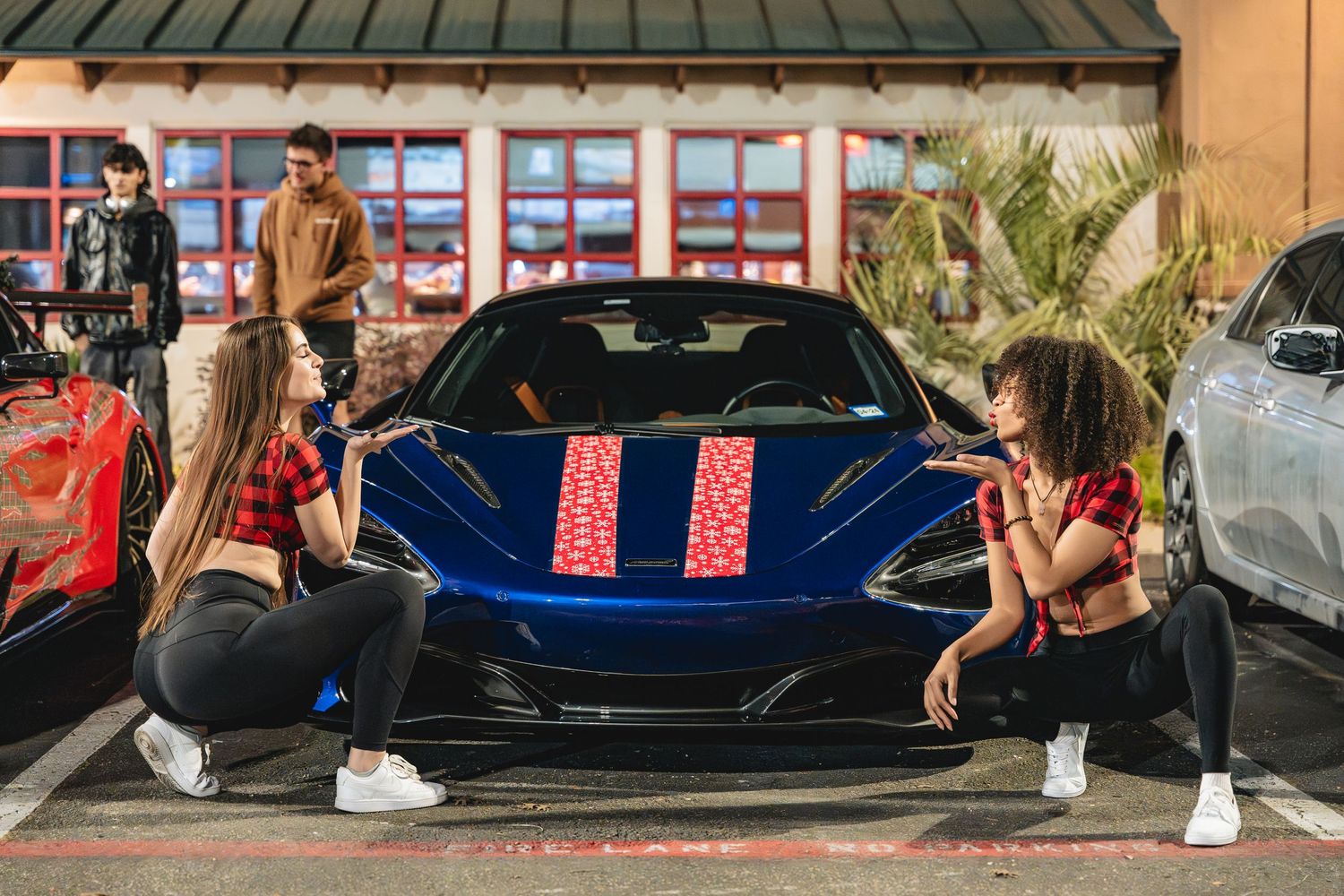 Two people strike poses in front of a blue McLaren sports car.