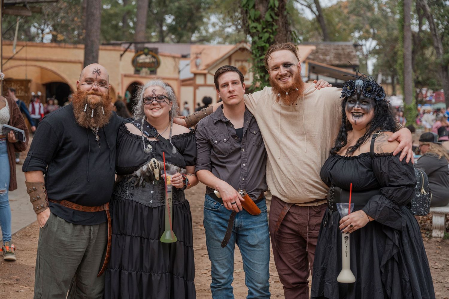 Group of renaissance faire attendees in period costumes posing together outdoors.