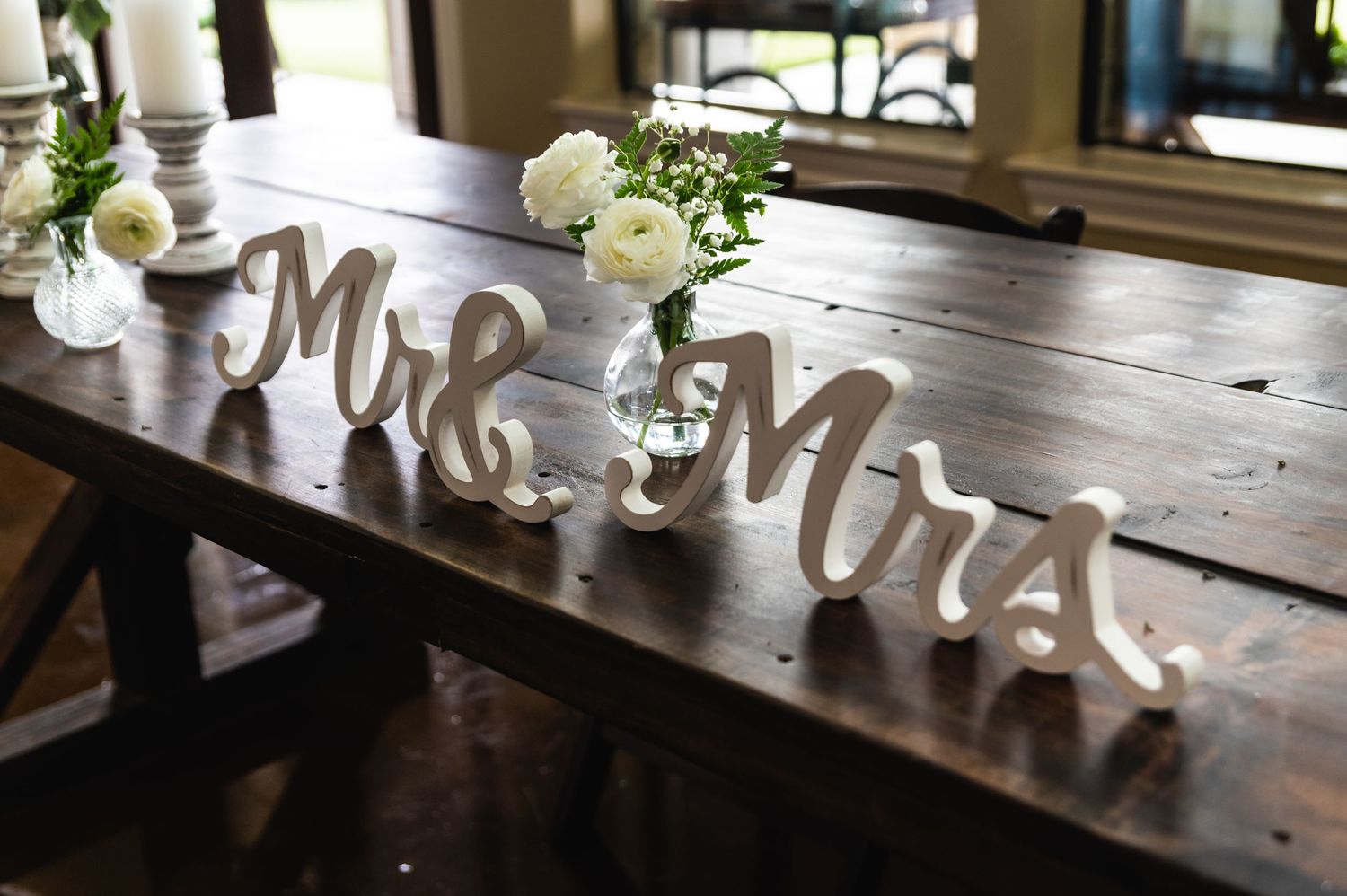 Mr and Mrs wooden letters displayed on rustic table with white roses in vases.