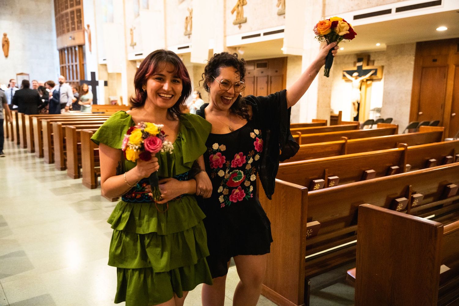 Two people celebrate in a church holding colorful bouquets and wearing festive attire.