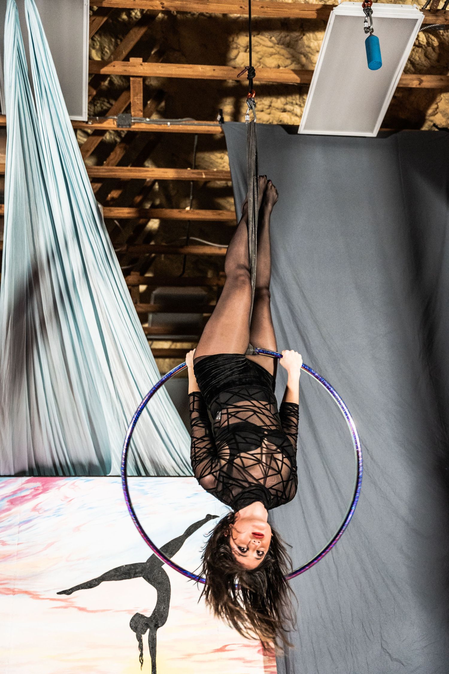 An aerial artist performs an inverted pose on a lyra hoop in a studio setting.