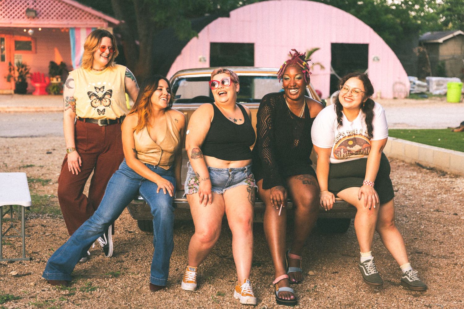 A group poses casually in front of a pink airstream trailer during a summer gathering.