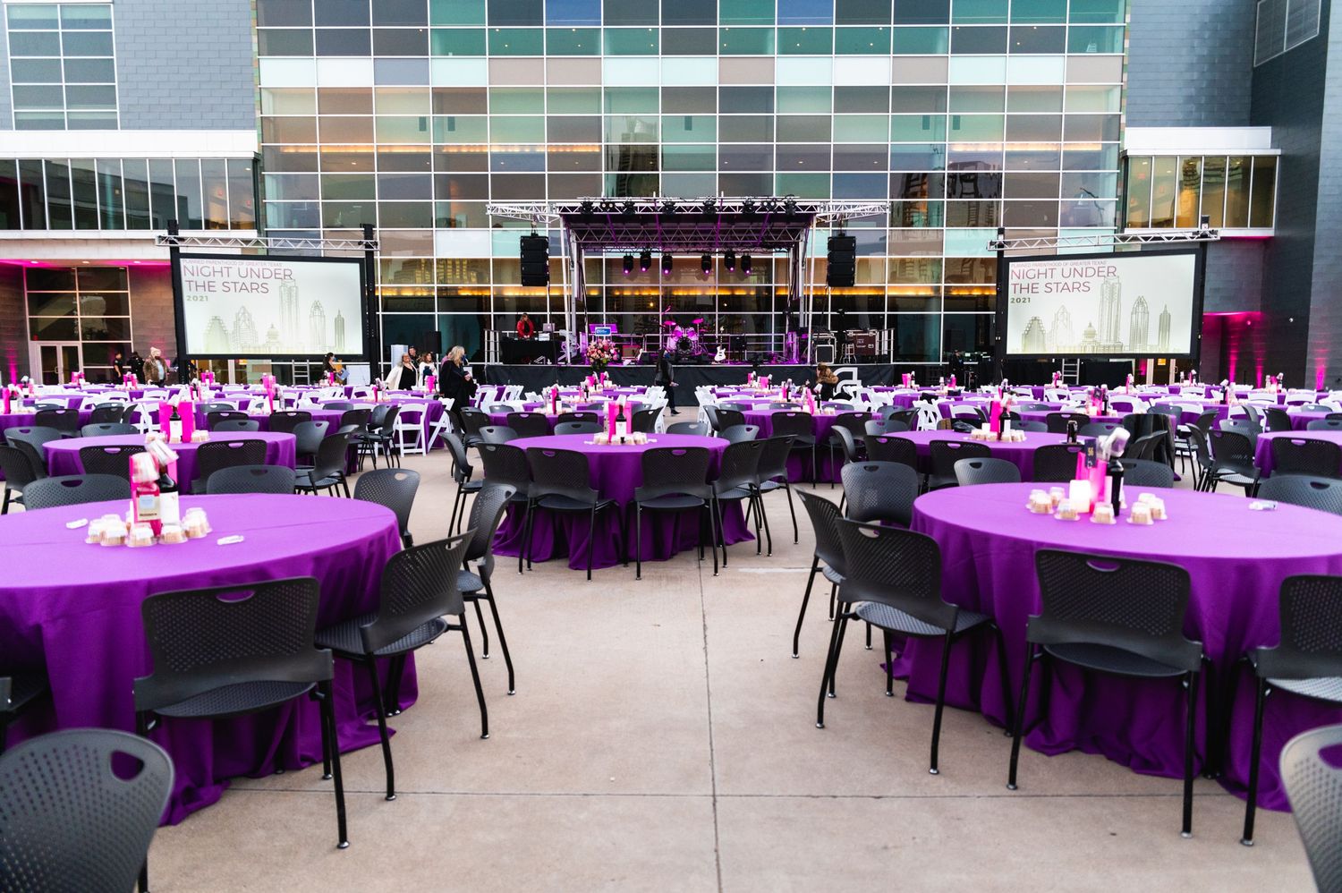 Event venue with rows of round tables covered in purple linens and projection screens.