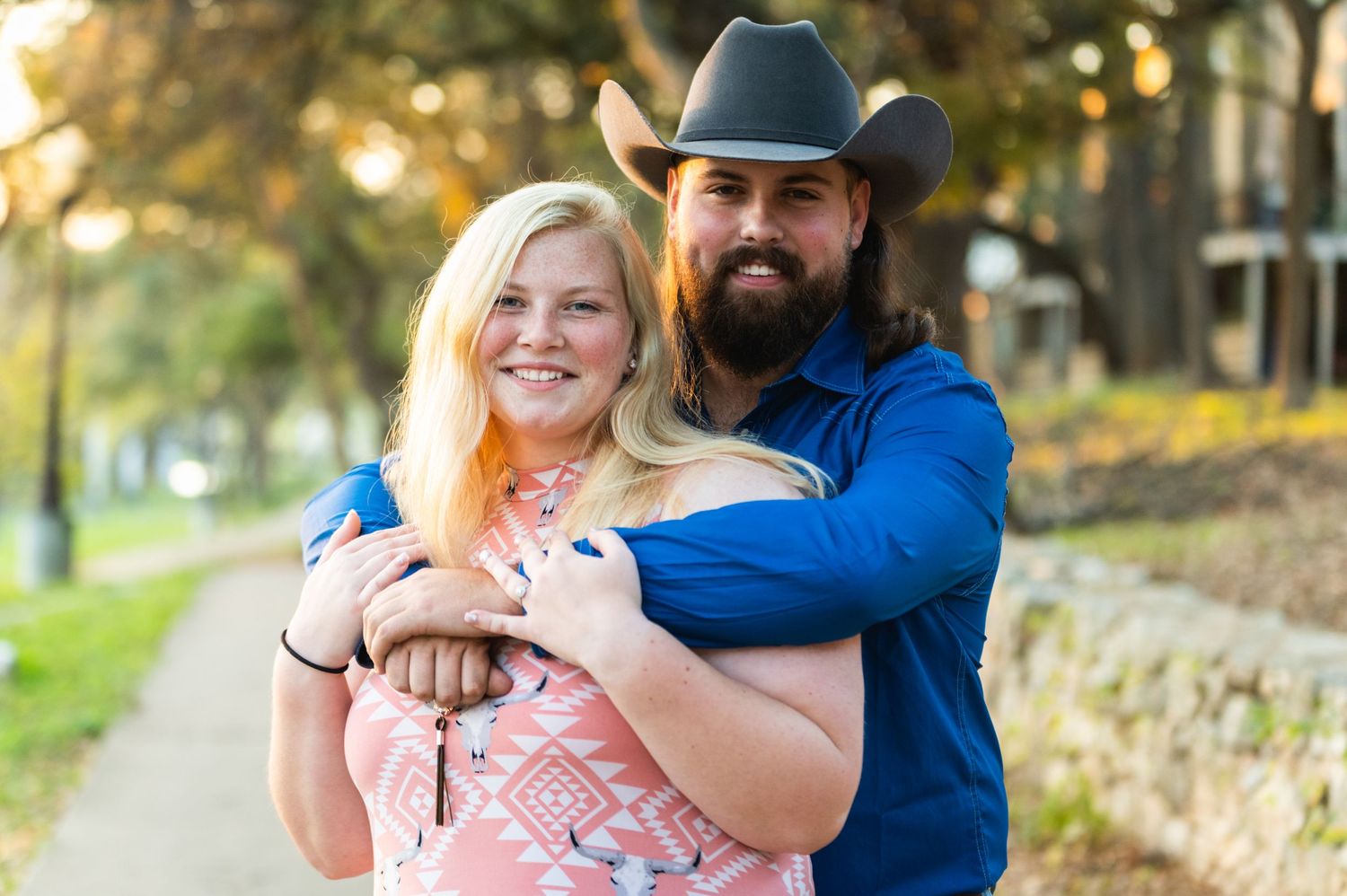 A couple in western attire embraces during an outdoor photo session.