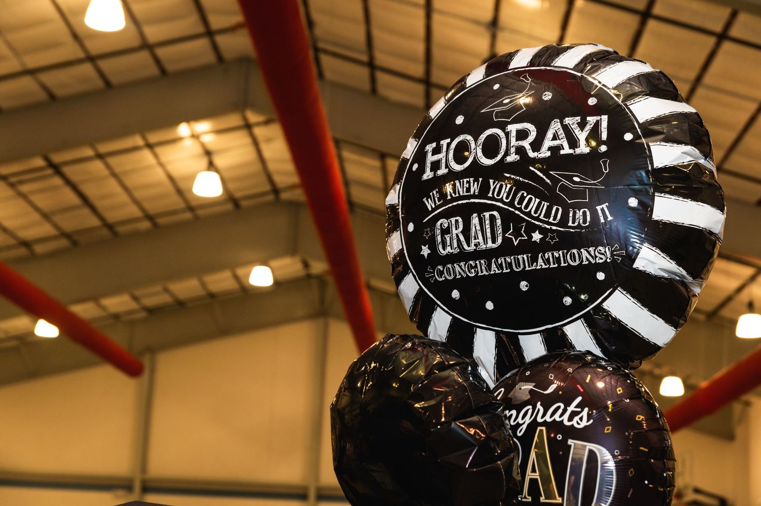 Black and silver graduation celebration balloons with 'HOORAY' text against ceiling.