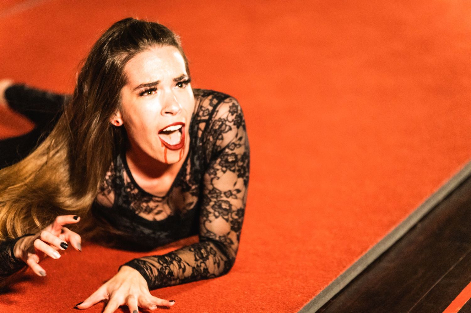 Dramatic pose on red stage floor with black lace costume.