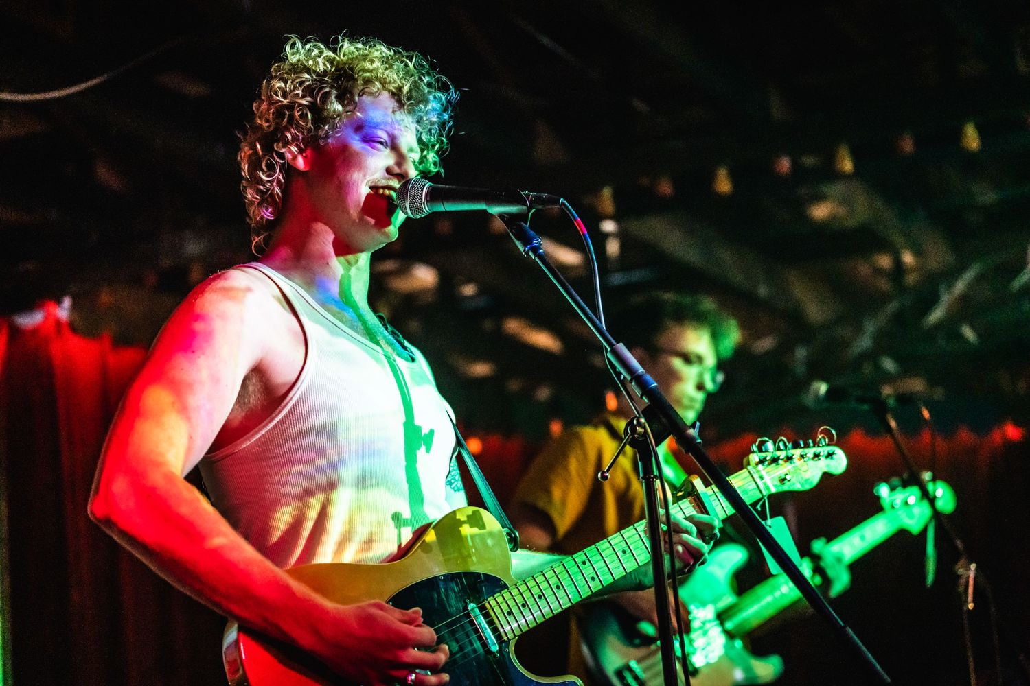 Musician performs on stage with a guitar under colorful lighting effects.