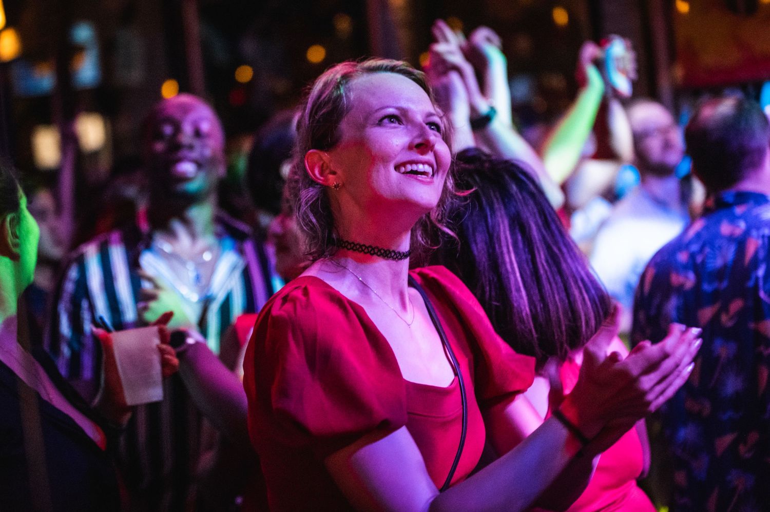 Energetic crowd enjoying live music with colorful stage lighting at an intimate concert venue.