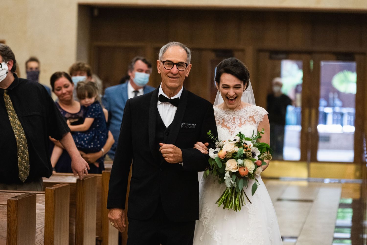 Wedding processional in traditional church with wooden pews and stained glass windows.