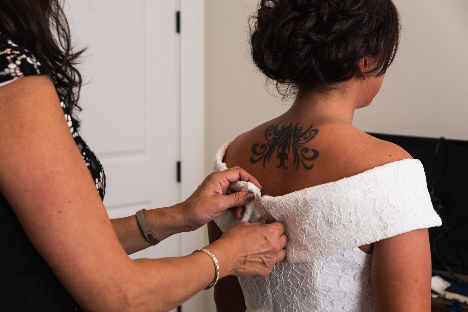 Hands adjusting the back of a white lace wedding dress, showing intricate details.