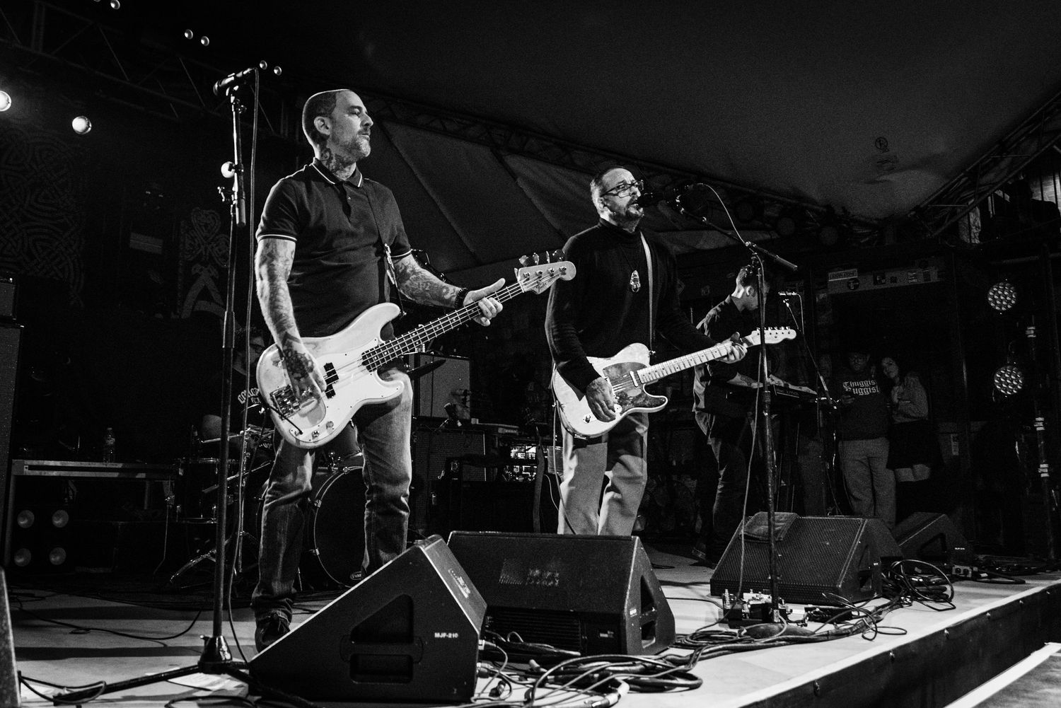 Black and white shot of band members performing with guitars on outdoor concert stage.