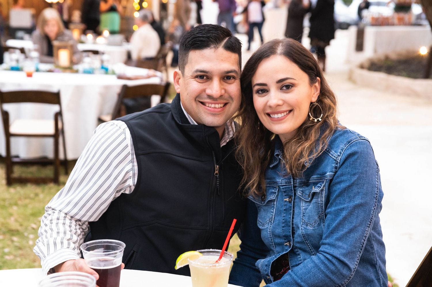 Couple enjoying drinks together at outdoor event with tables and chairs visible.