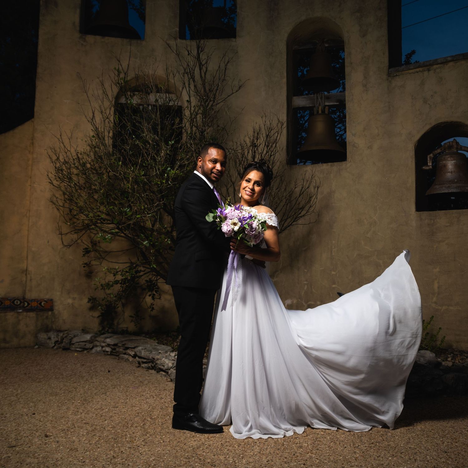 Elegant wedding portrait with the bride's dress flowing in the wind against adobe church walls.