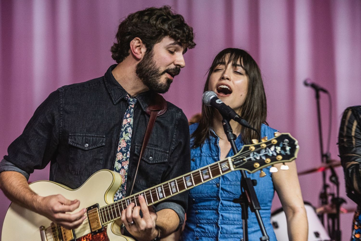 Musicians perform duet with guitars against purple stage curtain during live show.