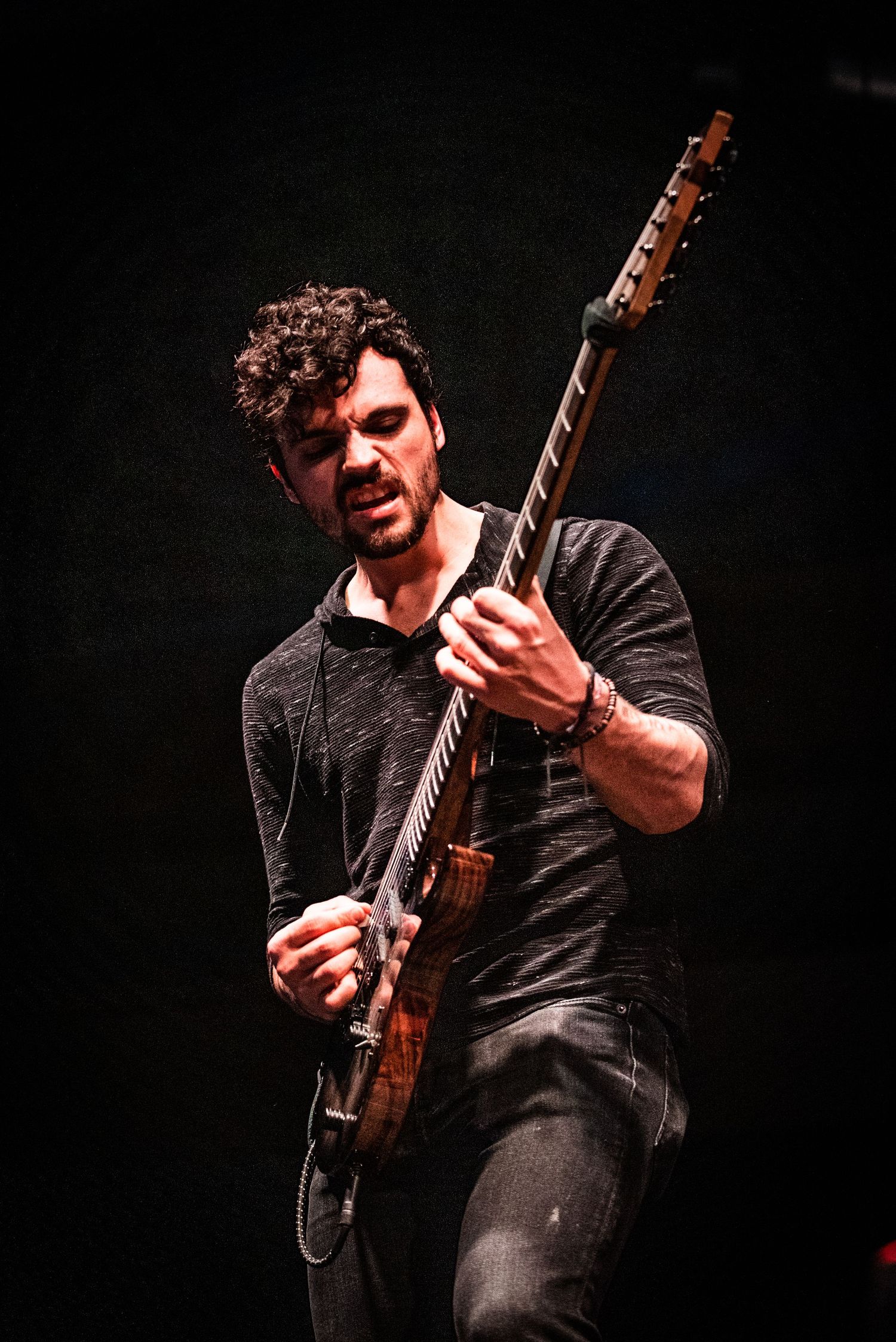 Guitarist with curly hair performs passionately on stage with electric guitar under warm lighting.