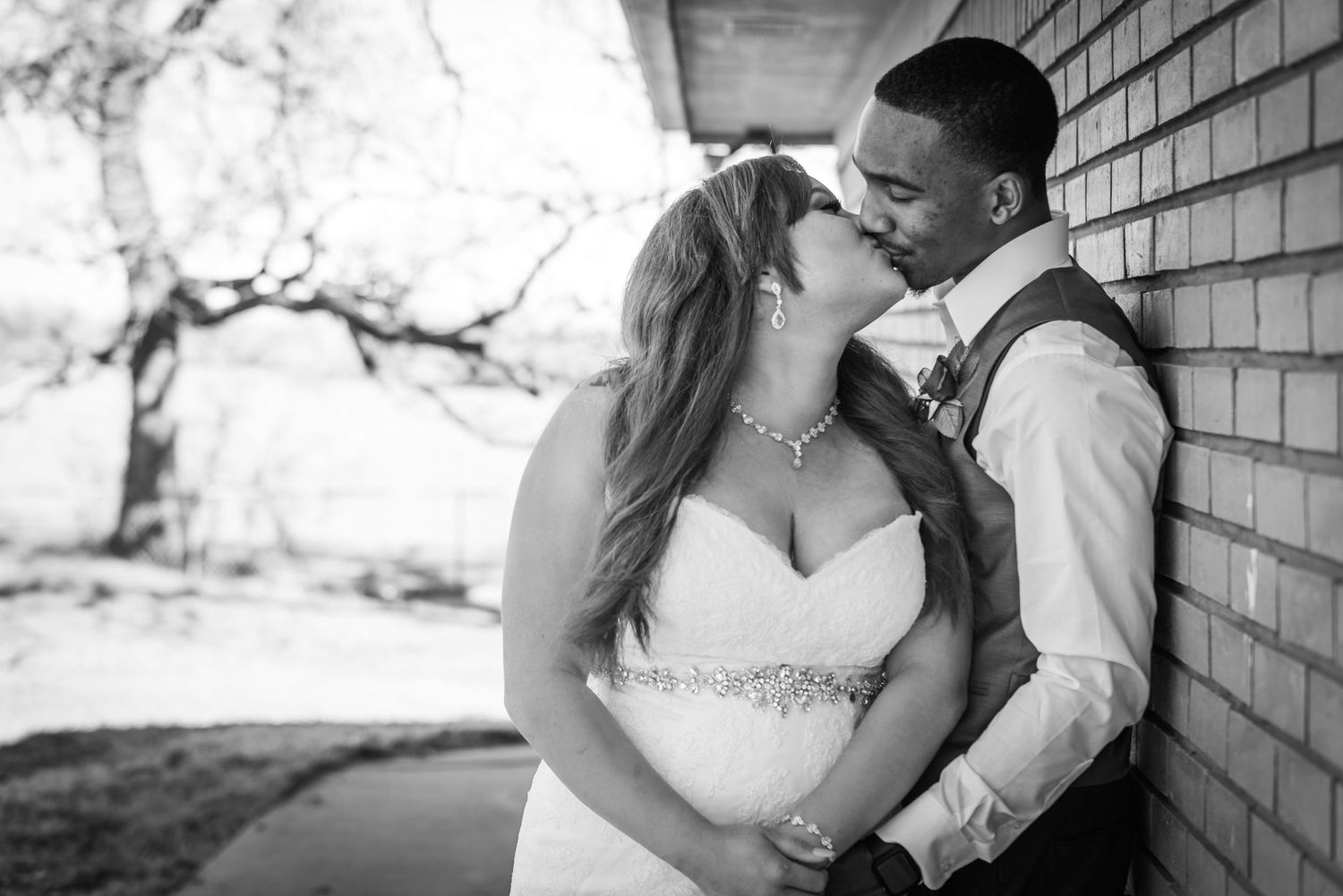 Black and white portrait of newlyweds sharing an intimate moment against brick wall.