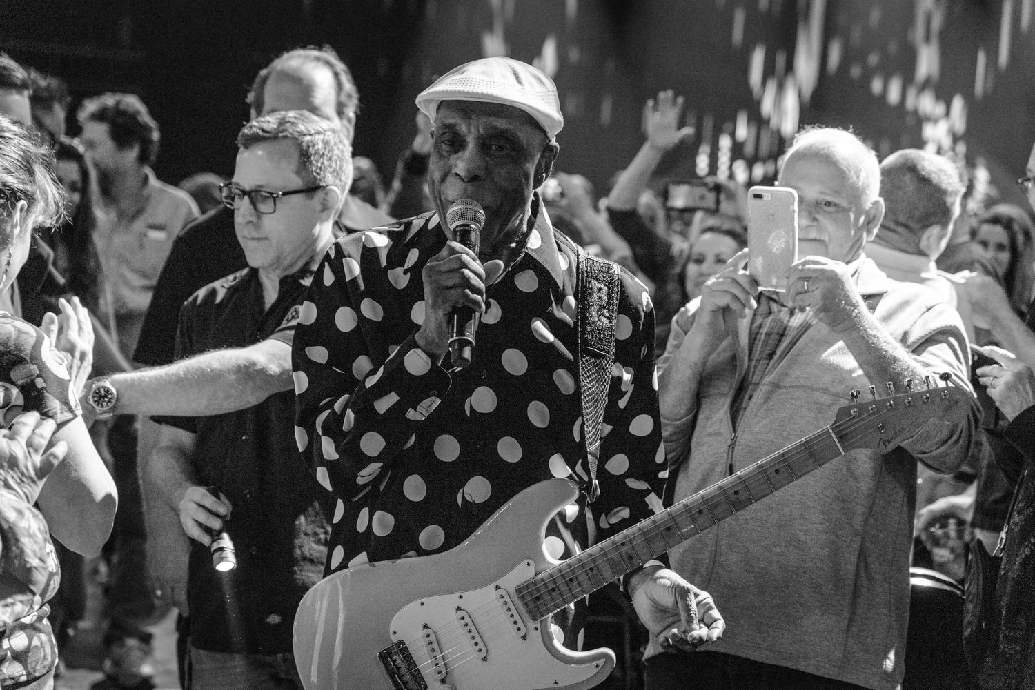 Black and white photo of musicians performing outdoors with crowd visible in background.