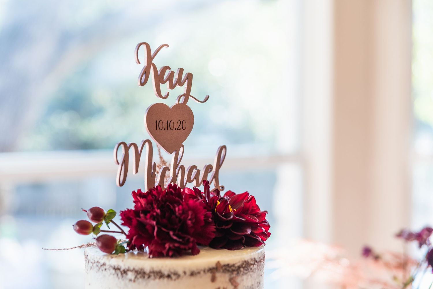 Wedding cake topper with names Kay and Michael decorated with deep red flowers.