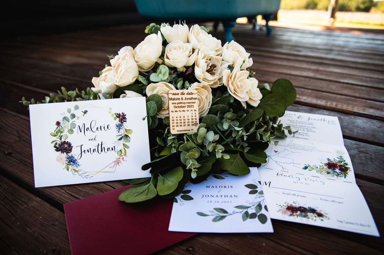 Wedding stationery and floral centerpiece with white roses displayed on dark wooden table.